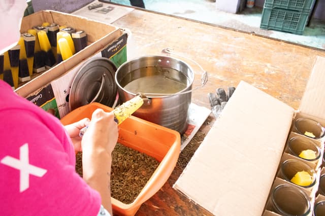 Manos cubriendo una veladora con hierbas secas sobre una charola