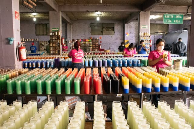 Trabajadoras terminando veladoras entre mesas llenas de piezas de colores