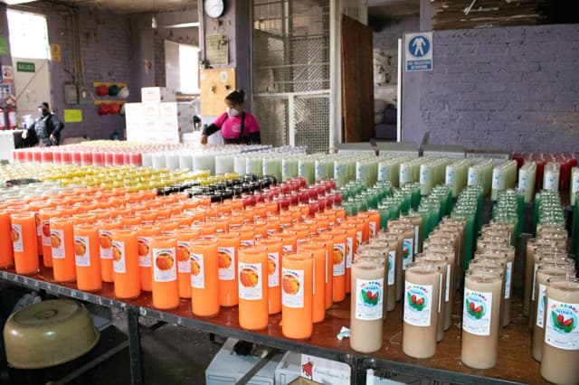 Filas de veladoras naranjas, verdes y blancas listas en el taller